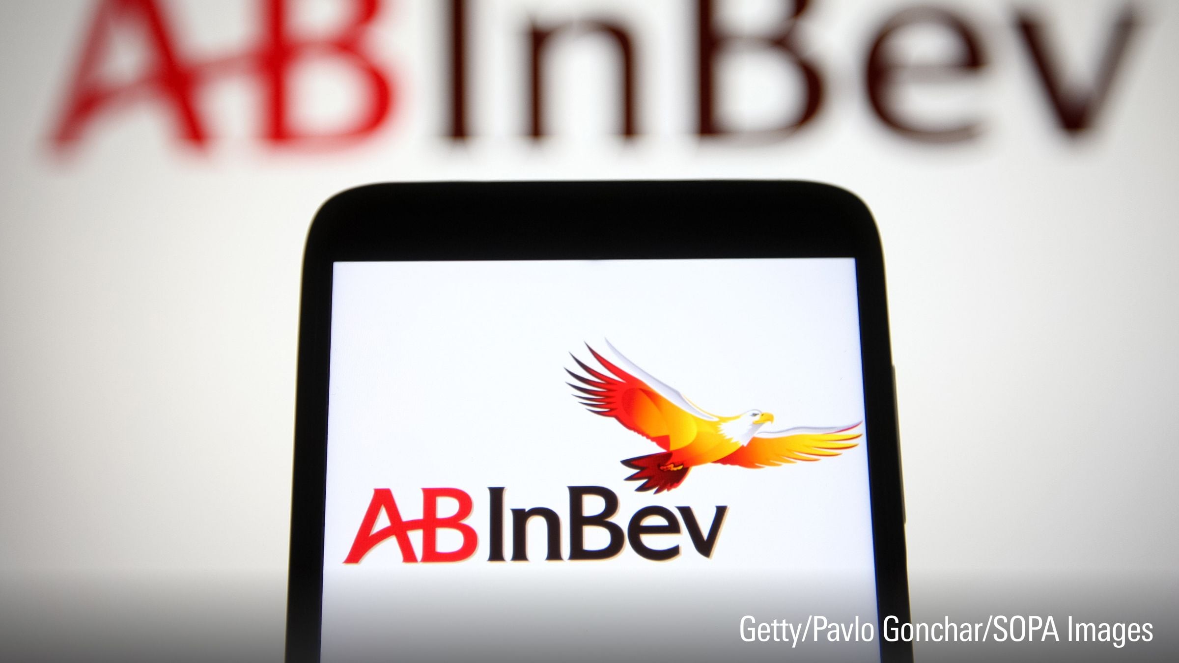 Op deze foto-illustratie is een logo van AB InBev (Anheuser-Busch InBev) te zien op een smartphone en een pc-scherm.